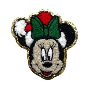 May include: Embroidered patch of a cartoon mouse face, wearing a red and white Santa hat and a green bow. The mouse has a beige face, black ears, and a gold glitter border. Suitable for application on clothing or accessories.