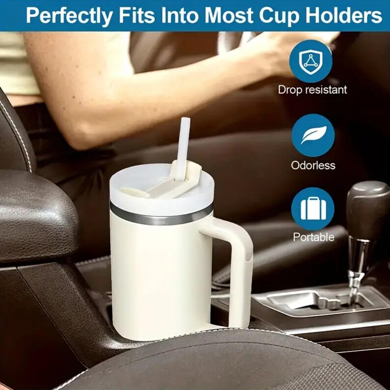May include: A cream-colored travel mug with a white lid and handle, featuring a white straw. The mug is in a car cup holder. Text on the image reads "Perfectly Fits Into Most Cup Holders". Additional icons indicate the mug is drop resistant, odorless, and portable.