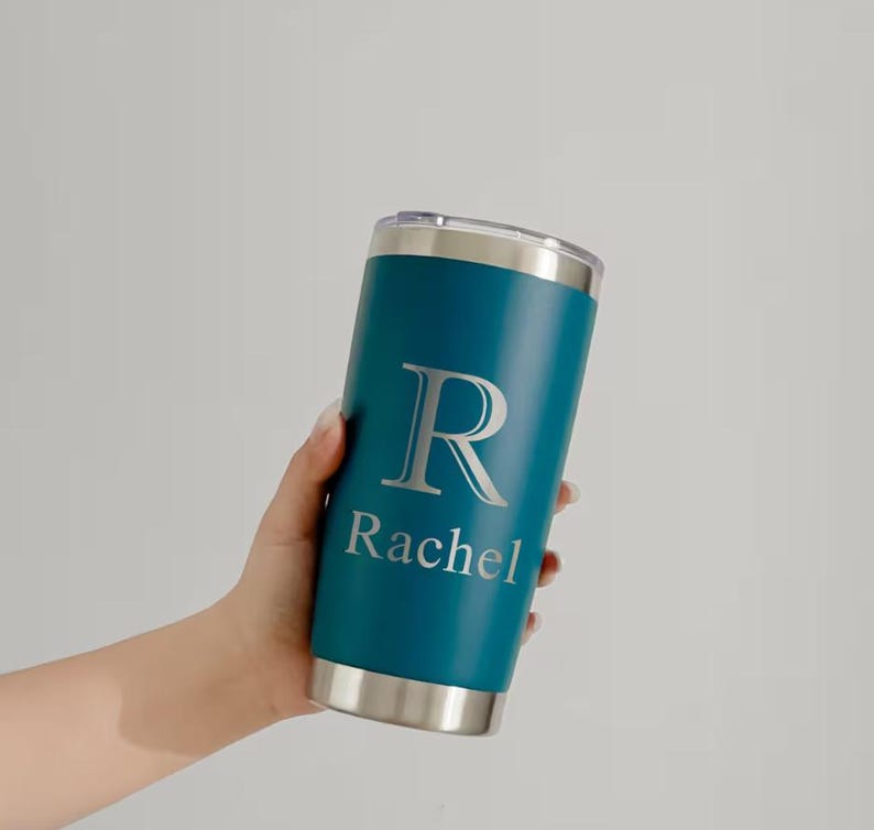 May include: Teal insulated tumbler with a silver lid and base. The tumbler features a large silver letter "R" and the name "Rachel" printed below. The tumbler is cylindrical and appears to be made of stainless steel.