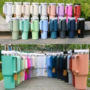 May include: A collection of insulated travel mugs in various colors, including white, beige, pink, red, and blue. Each mug has a handle, a lid, and a straw. The mugs are designed to keep beverages hot or cold.