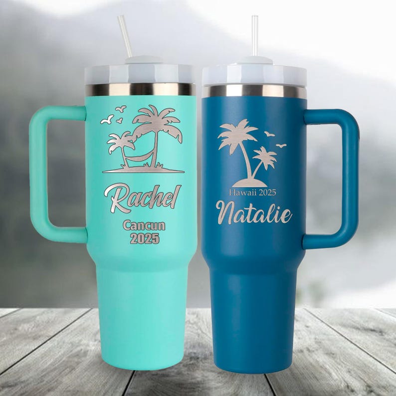 May include: Two insulated travel mugs with handles. One is teal with "Rachel Cancun 2025" and a palm tree design. The other is blue with "Hawaii 2025 Natalie" and a palm tree design. Both have white lids and straws.