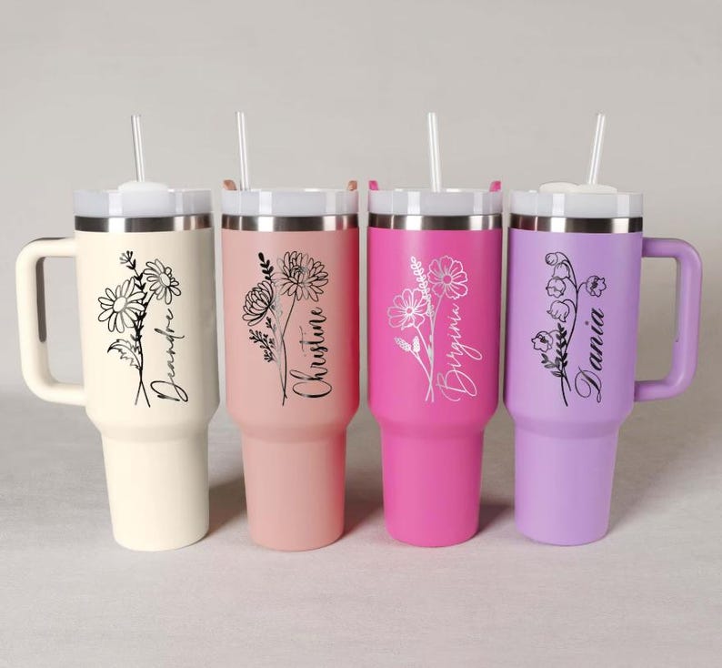 May include: Four insulated tumblers with handles and straws. The tumblers are in cream, pink, hot pink, and lavender. Each tumbler features a floral design and a name in script. The cream tumbler says "Deandre", the pink tumbler says "Christine", the hot pink tumbler says "Virgina", and the lavender tumbler says "Dania".