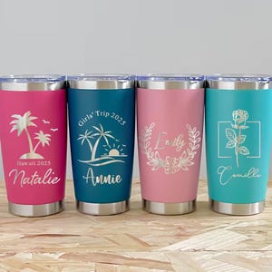 May include: Four stainless steel tumblers in pink, teal, and blue. Each tumbler features a unique design and name, including a palm tree, a rose, and floral accents. The text includes "Hawaii 2025", "Girls' Trip 2025", and names.