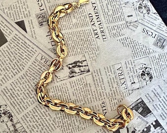 May include: A gold-colored chain bracelet with an oval link design. The bracelet is displayed on a newspaper background with the words "EXTRA" and "ART AND ITERTAIMENT" visible. The bracelet has a lobster clasp.