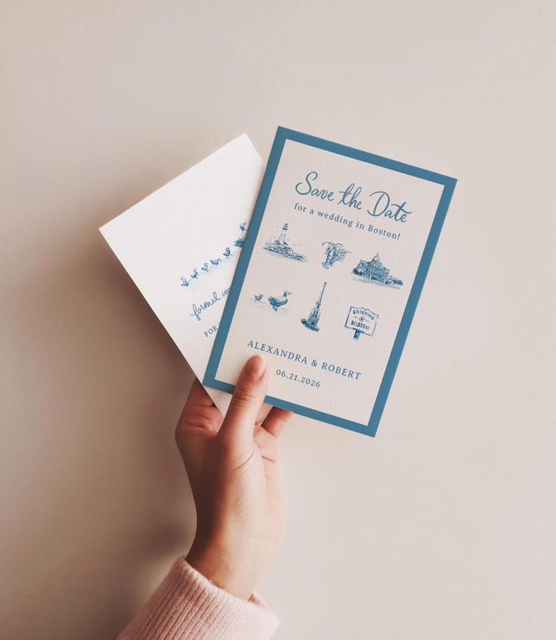 K&ouml;nnte beinhalten: Eine blau-wei&szlig;e Hochzeitseinladung mit dem Text "Save the Date" und Illustrationen von Wahrzeichen von Boston. Die Einladung enth&auml;lt die Namen "Alexandra & Robert" und das Datum "06.21.2026". Ein passender Umschlag ist ebenfalls zu sehen.