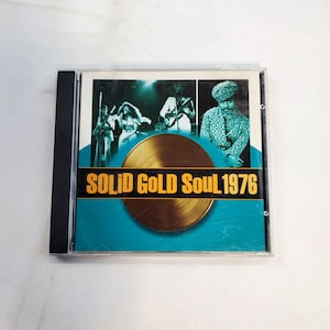 May include: A CD case featuring the album "Solid Gold Soul 1976." The cover has a teal background with a gold disc graphic and the album title in gold lettering. The top portion shows a band performing.