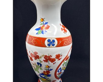 May include: White ceramic vase with a flared top and a round base. The vase features red and gold bands, and is decorated with colorful floral and foliate designs. The vase is approximately 20 cm tall.