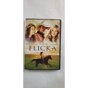 May include: DVD case for the film "Flicka" with Alison Lohman, Tim McGraw, and Maria Bello. The cover art depicts the actors and a girl riding a horse. The title "Flicka" is in gold lettering.