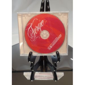May include: A CD in a clear plastic case. The CD has a red background with the name "Fergie" in white cursive script. The CD is displayed on a black easel.