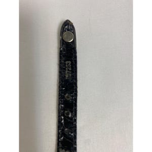 Op de afbeelding: Close-up van een zwart horlogebandje met een zilveren metalen sluiting. De band heeft een textuur, krokodilachtig patroon. Het nummer "97253" staat op de band.