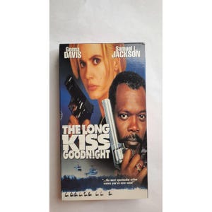 Puede incluir: Una cinta VHS de la película de acción "The Long Kiss Goodnight" con Geena Davis y Samuel L. Jackson. La portada muestra a los actores sosteniendo armas sobre un fondo azul oscuro con el título de la película en letras blancas grandes.