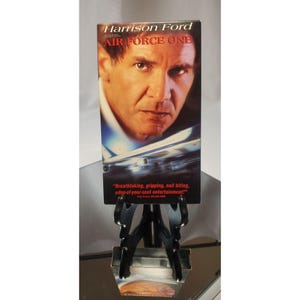 May include: A VHS tape for the movie "Air Force One" starring Harrison Ford. The cover features a close-up of Ford's face and an image of an airplane. The text on the cover reads "Air Force One".