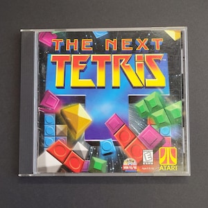 May include: A CD-ROM case for "The Next Tetris" video game. The cover features the game's title in yellow and red, with colorful geometric shapes. The game is rated "Everyone" by the ESRB and published by Atari.
