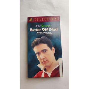 May include: A VHS tape for the movie "Better Off Dead" featuring John Cusack. The cover has a blue background with the movie title in large, bold letters. The text "Teenage life has never been darker...or funnier" is also visible.