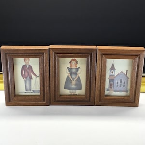 May include: Set of three framed prints with a rustic brown wooden frame. The prints depict a boy with a sailboat, a girl with a basket, and a church. The artwork features soft colors and a vintage aesthetic, suitable for home decor.