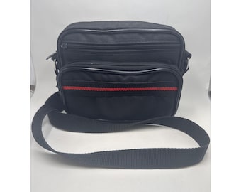 May include: Black messenger bag with a red stripe detail. The bag has a rectangular shape with multiple zipped compartments and a long, adjustable shoulder strap. The bag is made of a durable material and is suitable for everyday use.