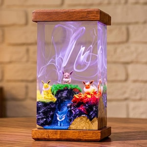 May include: A rectangular lamp with a wooden frame and base, featuring a colorful diorama inside. The diorama depicts cartoon characters on a landscape with waterfalls and colorful terrain. The lamp's interior has a swirling, smoky design.