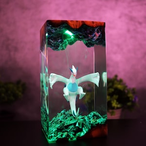 May include: A rectangular resin art piece featuring a white and blue dragon figurine. The artwork has a green, glowing base and top, with a red and blue border. The dragon is centered within the clear resin, creating a unique display.