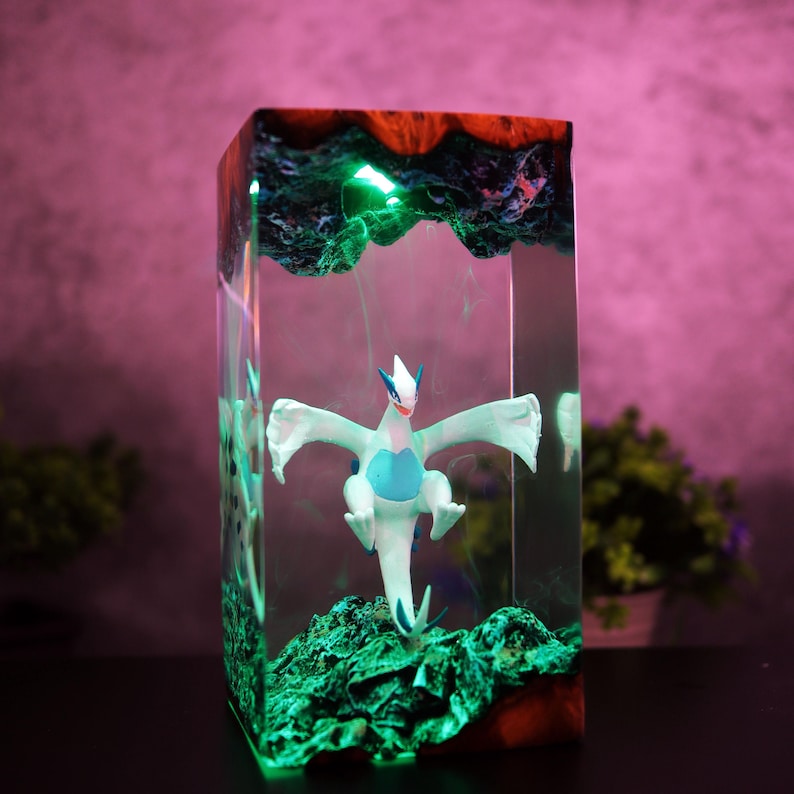 May include: A rectangular resin art piece featuring a white and blue dragon figurine. The artwork has a green, glowing base and top, with a red and blue border. The dragon is centered within the clear resin, creating a unique display.