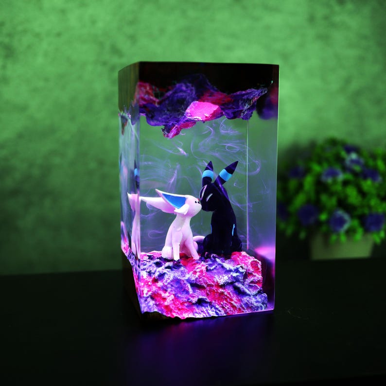 May include: A rectangular resin sculpture featuring two stylized animal figures in a loving embrace. The sculpture has a vibrant color palette of pink, purple, and blue, with a glowing effect. The background is a gradient of green.