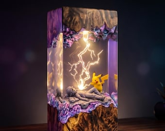 May include: A rectangular resin and wood lamp featuring a yellow Pikachu figure standing next to a reclining grey figure. The interior is illuminated by a bright, jagged lightning bolt effect, surrounded by purple and brown textured wood elements.