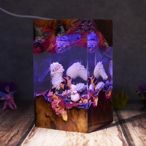 May include: A wooden block with a clear resin interior, featuring figurines of a creature with orange and black stripes and white fur. The resin is illuminated with purple light, and the base has a natural wood grain.
