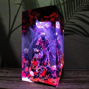 Può includere: Una scultura rettangolare in resina con una figura all'interno. La scultura presenta una base rossa e nera con una figura in un abito rosso e nero. L'interno ha un design a vortice viola e bianco, con una parte superiore rossa e nera.