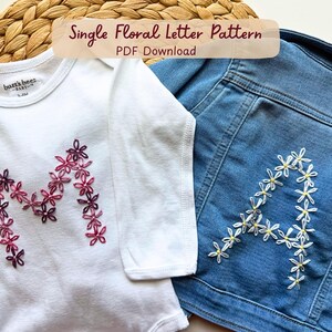 May include: A white long-sleeve bodysuit featuring a letter M embroidered with pink and purple floral stitches, alongside a blue denim jacket with a letter A embroidered with white and yellow floral stitches. Text reads Single Floral Letter Pattern.