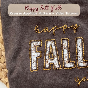 May include: A dark brown sweatshirt featuring the text Happy Fall Y'all. The word happy is embroidered in yellow thread, the word FALL is in reverse applique with a white floral fabric, and the word y'all is embroidered in yellow thread.
