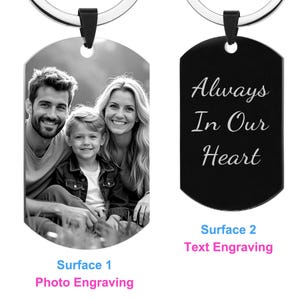 May include: Black and white photo engraved on a silver keychain with a black rectangular tag that says "Always In Our Heart" engraved on it.