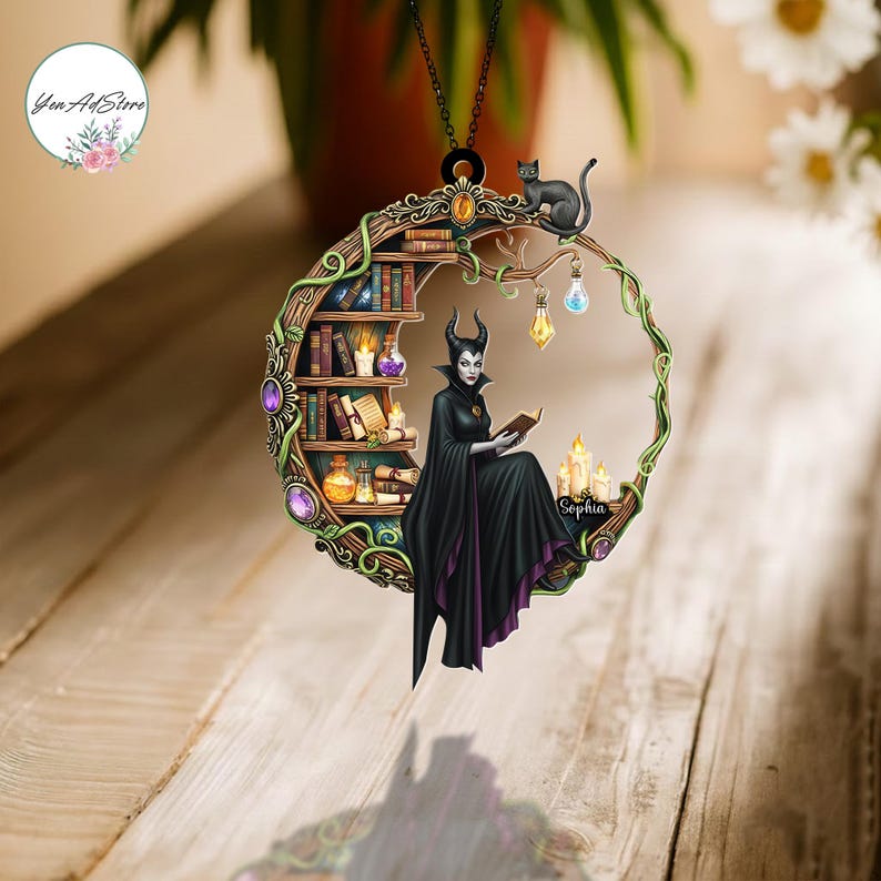 May include: A circular ornament featuring a fantasy scene with a woman in a black cloak reading a book. A black cat sits atop a branch. The ornament includes a bookshelf, candles, and the name "Sophia".