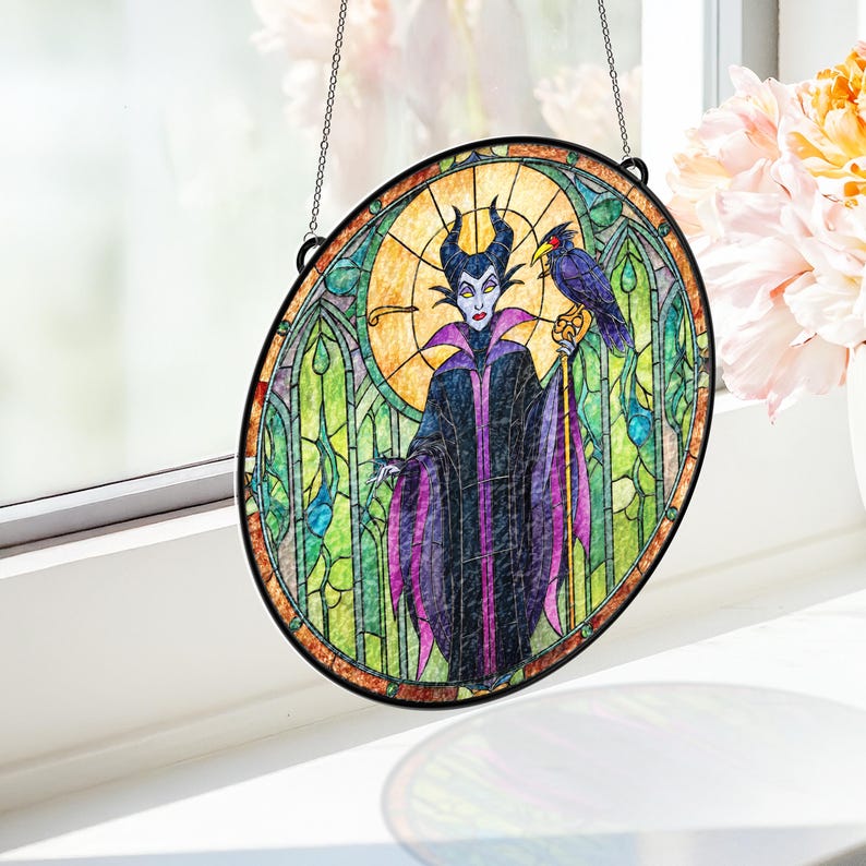 Pu&ograve; includere: Arte vetrata ovale raffigurante un personaggio dei cartoni animati con corna nere, un mantello viola e nero e un corvo. L'opera d'arte ha un bordo nero ed &egrave; sospesa da una catena. Lo sfondo include un sole giallo e vetrate verdi.