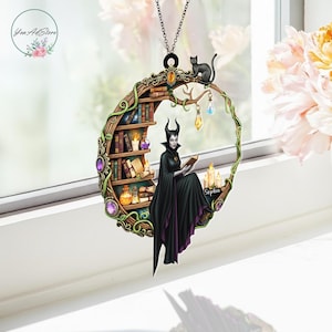 May include: A circular pendant featuring a witch reading a book, with a black cat perched above. The design includes a bookshelf, candles, and decorative gems. The witch wears a black cape with purple trim. The pendant is suspended by a chain.