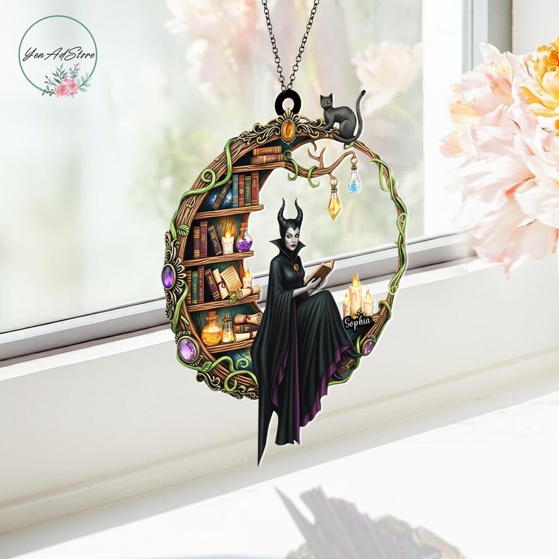 May include: A circular pendant featuring a witch reading a book, with a black cat perched above. The design includes a bookshelf, candles, and decorative gems. The witch wears a black cape with purple trim. The pendant is suspended by a chain.