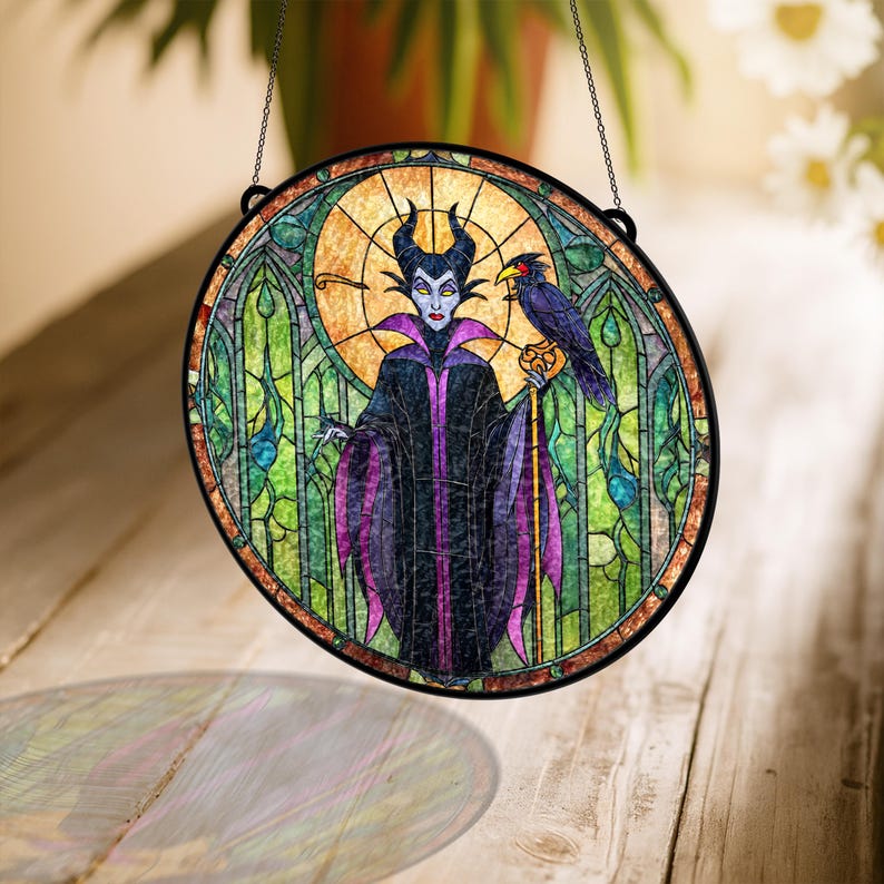 Pu&ograve; includere: Una vetrata rotonda con un'immagine stilizzata di un personaggio con corna nere, un abito viola e nero e un corvo. La finestra ha una cornice in metallo nero ed &egrave; sospesa da una catena. Lo sfondo &egrave; un mix di verde, giallo e arancione.