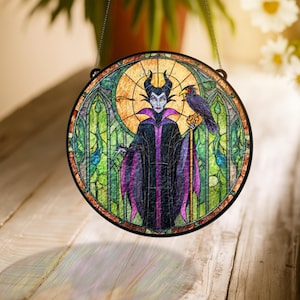 Pu&ograve; includere: Vetrata rotonda raffigurante un personaggio con corna nere, una veste viola e nera e un corvo. La finestra ha una cornice in metallo nero e una catena per appenderla. Lo sfondo &egrave; un mix di verde, giallo e arancione.