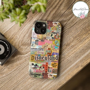 Puede incluir: Una funda de teléfono con un collage de imágenes vintage de Disneyland. El diseño incluye la palabra "Disneyland" en una fuente colorida, junto con varios gráficos y texto. La funda está sobre una superficie de madera.