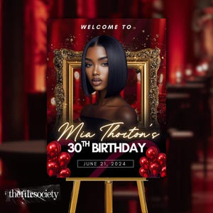 May include: A birthday party welcome sign featuring a woman's portrait inside a gold frame. The sign reads "Mia Thornton's 30th Birthday" with the date "June 21, 2024" and is decorated with red balloons. The sign is displayed on a wooden easel.