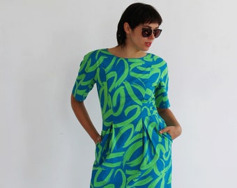 Puede incluir: Una mujer vistiendo un vestido azul y verde con un patrón abstracto. El vestido tiene manga corta y una silueta ajustada.