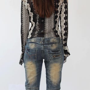 Puede incluir: Una blusa de manga larga con estampado blanco y negro con un pu&ntilde;o con volantes. La blusa se lleva con unos vaqueros azules desgastados.