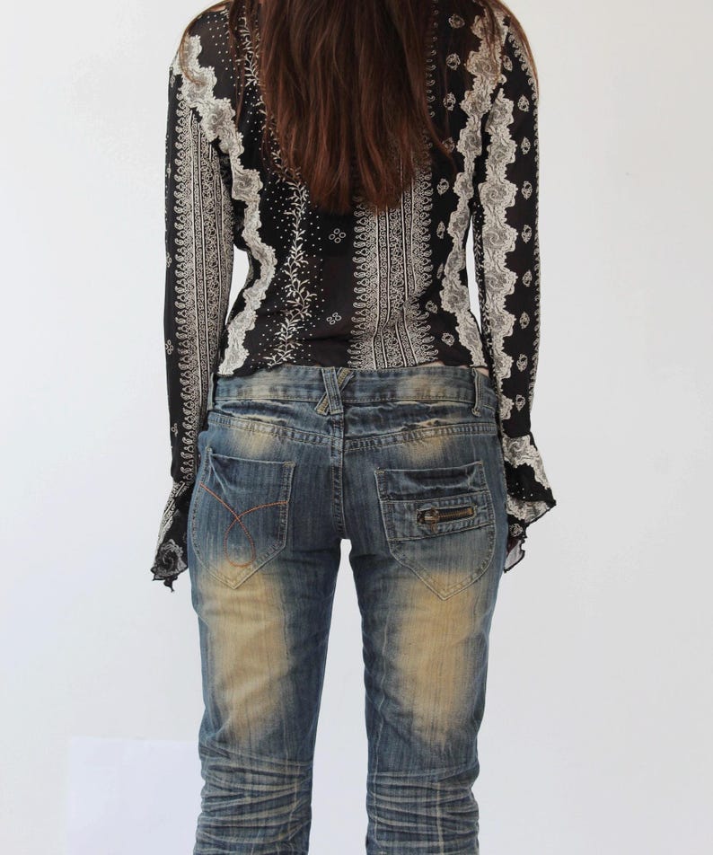 Puede incluir: Una blusa de manga larga con estampado blanco y negro con un pu&ntilde;o con volantes. La blusa se lleva con unos vaqueros azules desgastados.