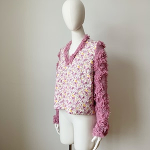 Può includere: Un cardigan rosa con stampa floreale e bordi rosa pelosi sulle maniche.