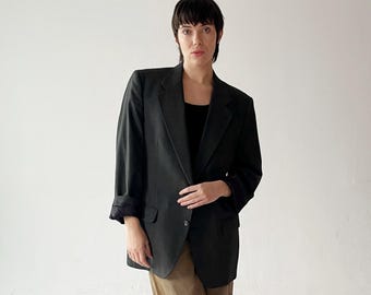 May include: A dark green blazer with a single button closure and a pocket on the left side. The blazer has a slightly oversized fit and is made of a textured fabric.