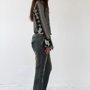 Puede incluir: Una mujer con una blusa de manga larga con estampado blanco y negro y unos vaqueros azules. Lleva zapatos marrones.