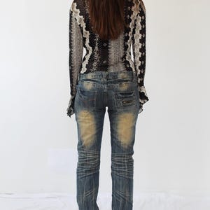 Puede incluir: Una mujer con una blusa de manga larga con estampado blanco y negro y un par de pantalones vaqueros azules con detalles desgastados.