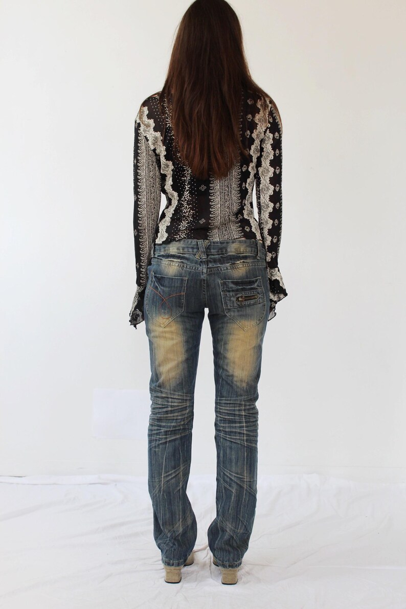 Puede incluir: Una mujer con una blusa de manga larga con estampado blanco y negro y un par de pantalones vaqueros azules con detalles desgastados.