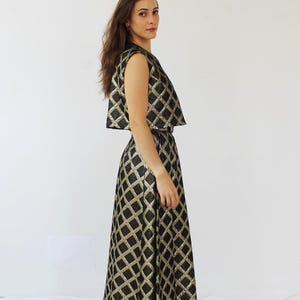 Pu&ograve; includere: Un completo formale a due pezzi con un top corto senza maniche e una gonna lunga. L'ensemble &egrave; nero con un motivo a rombi dorati. L'outfit &egrave; realizzato in un tessuto lucido.
