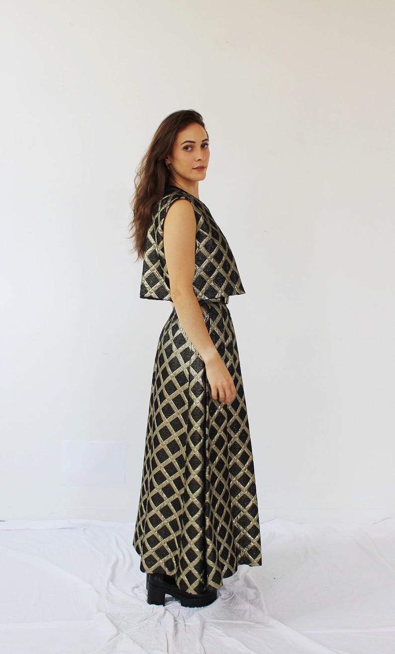 Pu&ograve; includere: Un completo formale a due pezzi con un top corto senza maniche e una gonna lunga. L'ensemble &egrave; nero con un motivo a rombi dorati. L'outfit &egrave; realizzato in un tessuto lucido.