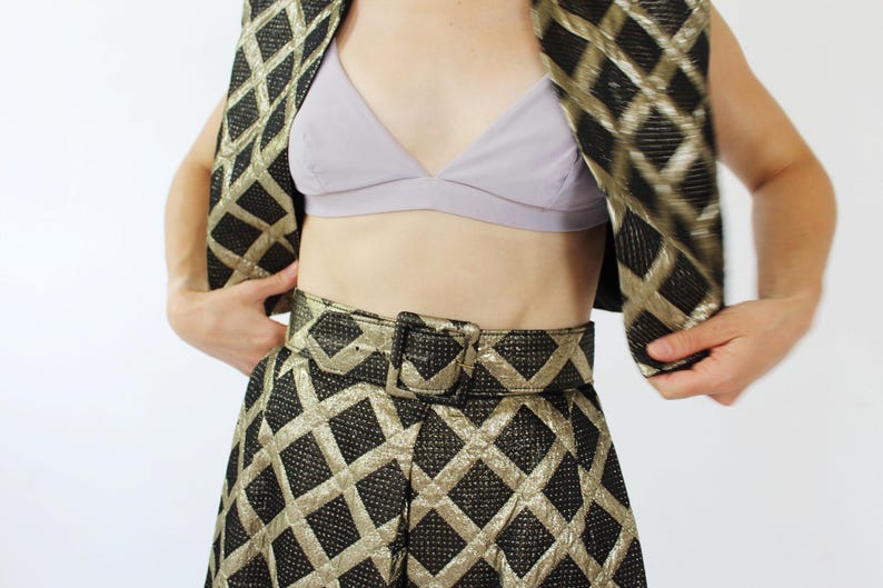 Pu&ograve; includere: Un completo composto da gilet, gonna e cintura con motivo nero e oro. Il gilet e la gonna presentano un motivo a rombi. La cintura ha una grande fibbia quadrata. Si vede un reggiseno color lavanda.