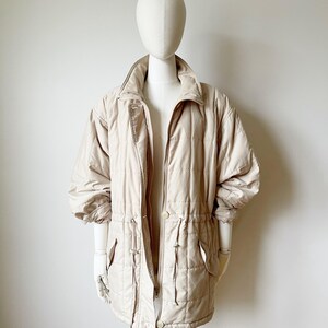 May include: A beige quilted jacket with a drawstring waist and a zipper closure.